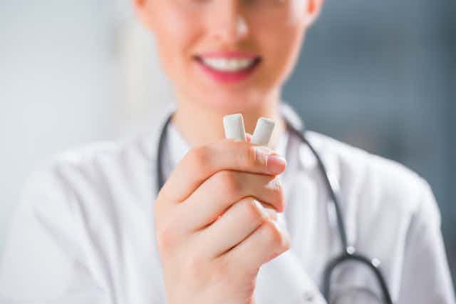 A doctor or dentist holds two pieces of chewing gum.