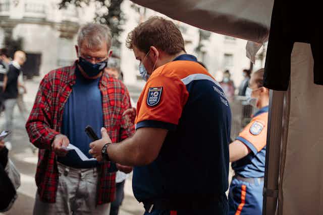 Man in blue and orange shirt holding smartphone while looking at paper vaccination passport