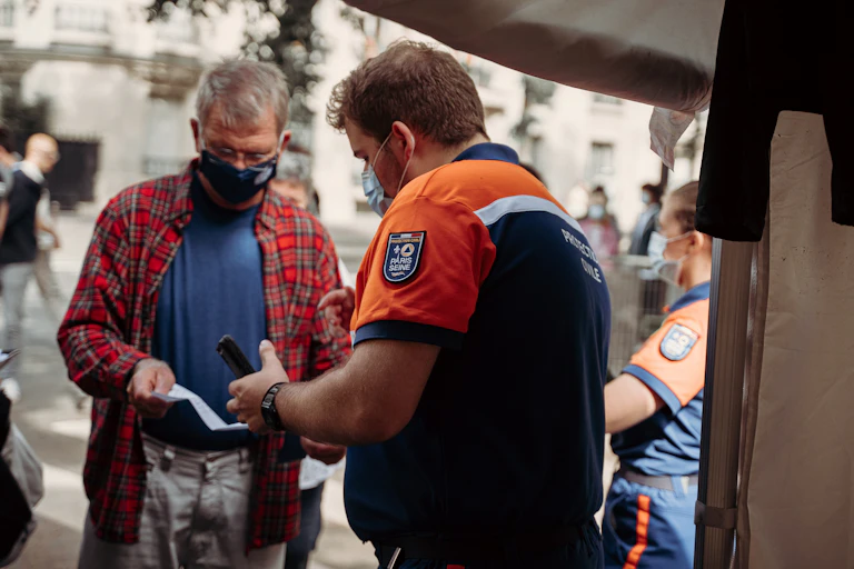 Man in blue and orange shirt holding smartphone while looking at paper vaccination passport