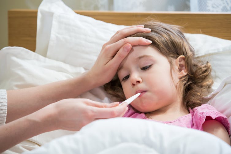 A child in bed having their temperature taken