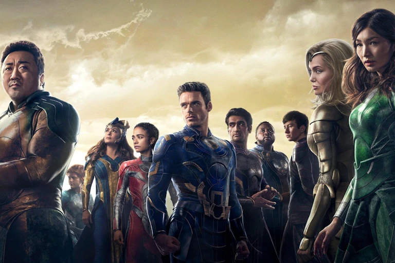 Cast of Eternals in a row in different coloured superhero outfits