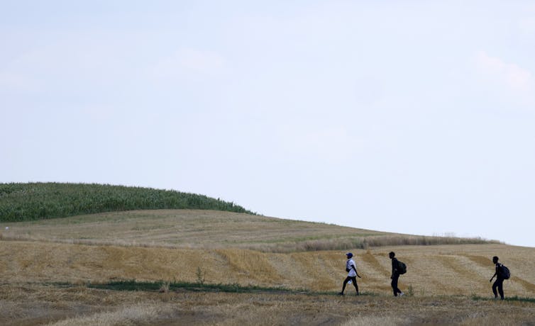 Three people walk in single file in an arid field.