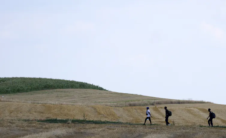 Three people walk in single file in an arid field.