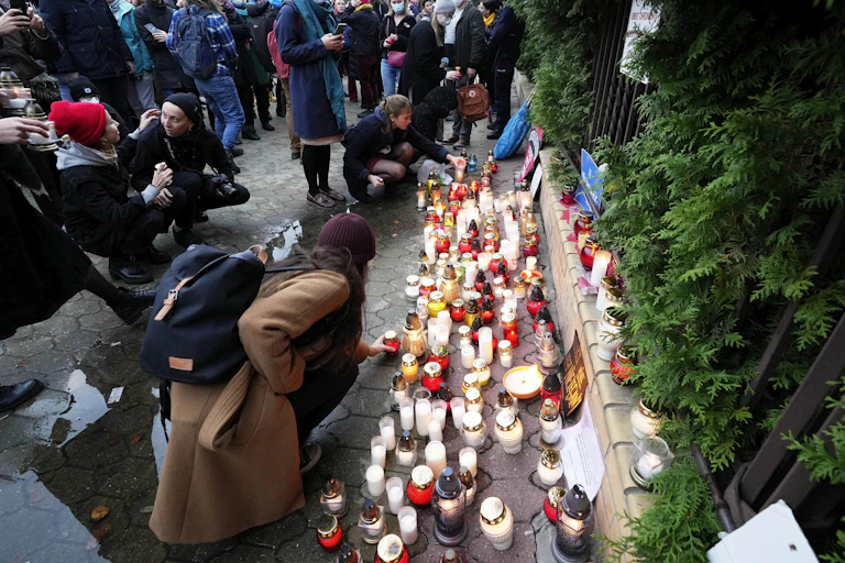 People light candles outside an iron gate. Some take photos.