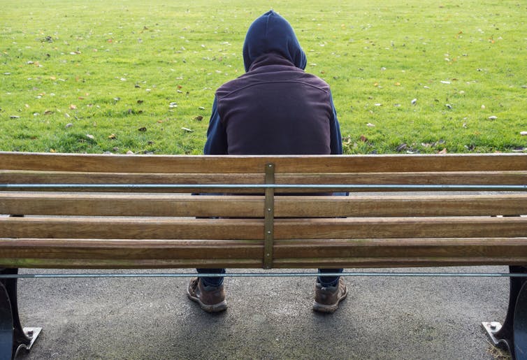 Young man sitting on his own on a park bench.