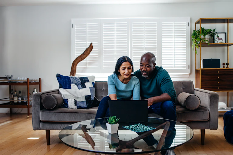 A middle-aged couple work on a shared laptop.