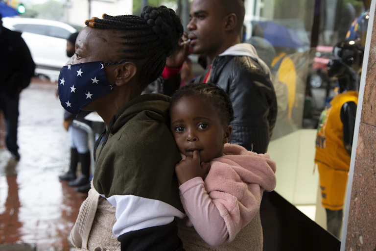 woman wears mask and carries baby in backpack