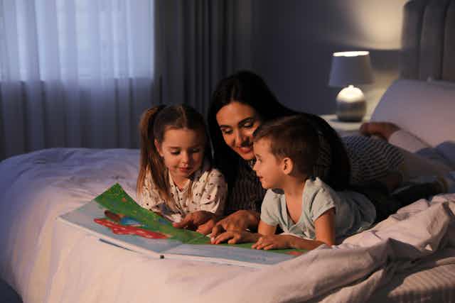 mother reading to young children on bed