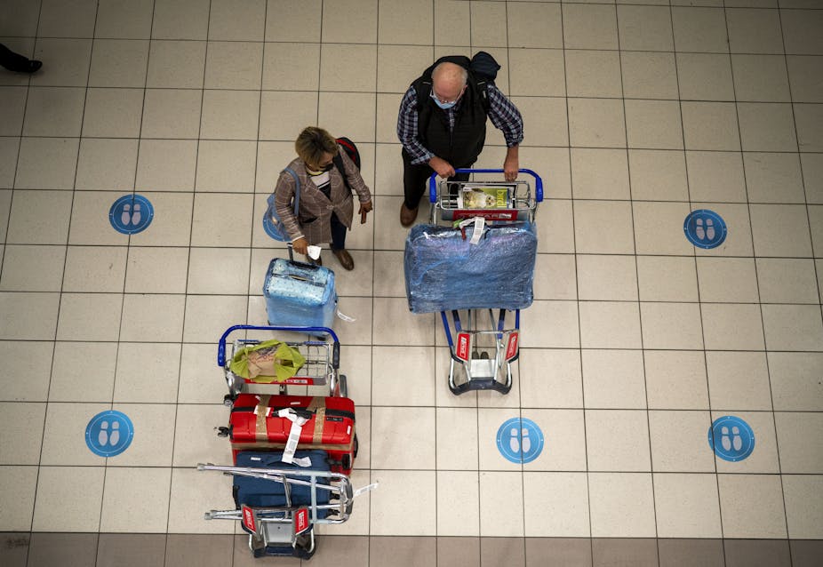 Two passengers in an airport, wearing masks to protect against COVID-19, stand with luggage carts.