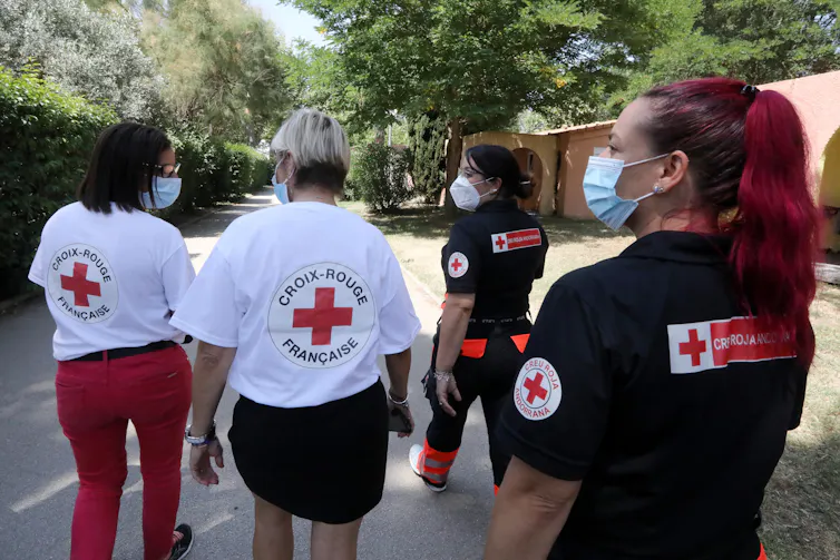 Des membres de la Croix-Rouge française marchent sur une allée pour rencontrer des vacanciers lors d’une campagne de sensibilisation à la vaccination contre le Covid-19 dans un camping, le 13 août 2021 à Argelès-sur-Mer, dans le sud de la France