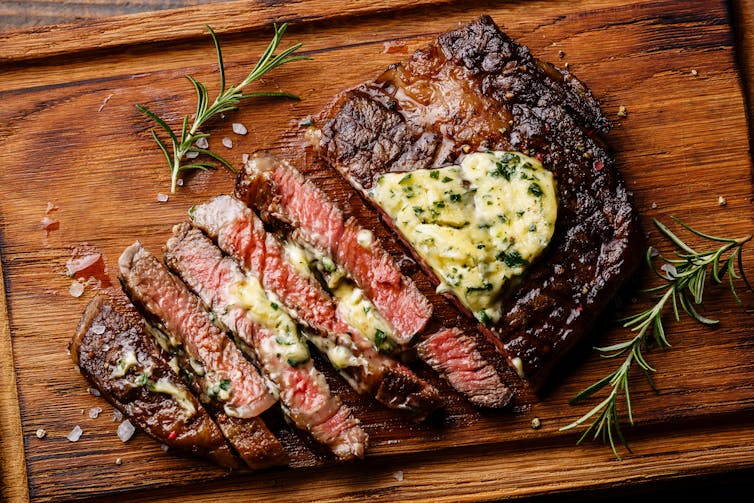 A medium-rare steak, sliced up on a wooden board and covered in butter.