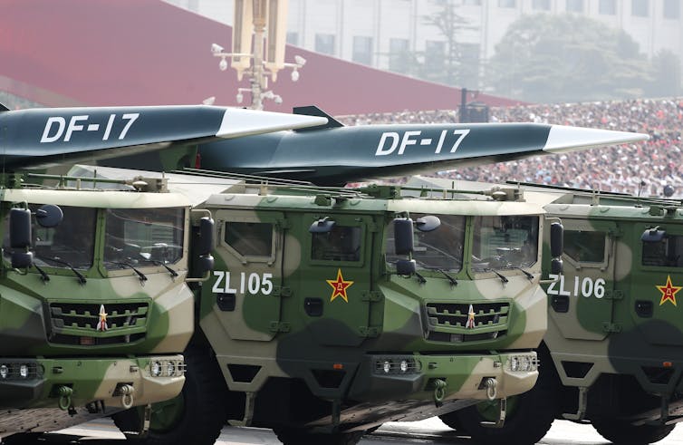 Missiles mounted on Chinese military trucks with crowd of people watching in background.