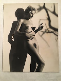A nude woman in a studio applies sun cream under the shadow of a tree