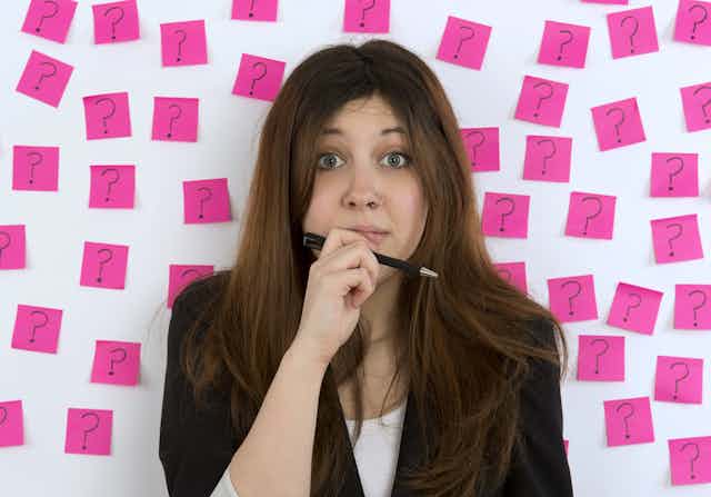 Young woman with nose ring with pink sticky notes and question mark thinking about decision making