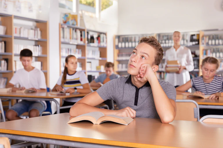 Teenage boy with book in class looking bored