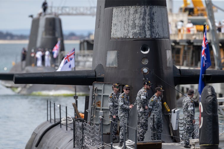 Military personnel stand on a submarine.