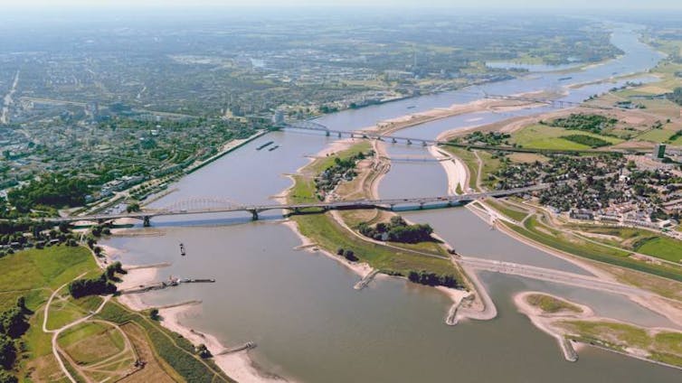 aerial view of a bend in a river with some elongated islands, several bridges and homes and business developments on each bank.