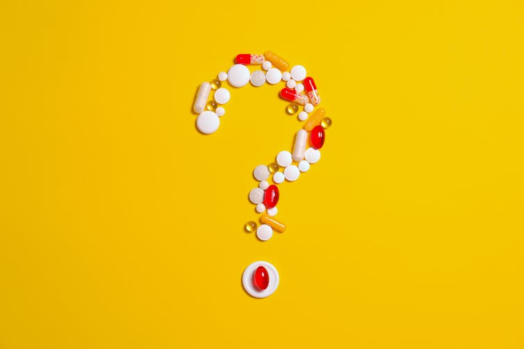Pills arranged in the shape of a question mark against a yellow background