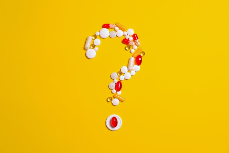 Pills arranged in the shape of a question mark against a yellow background