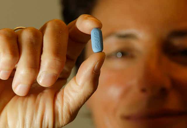 Person holding blue Truvada pill between two fingers.