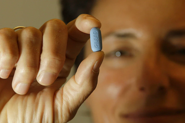 Person holding blue Truvada pill between two fingers.
