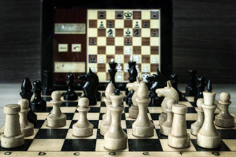 Chess board with pieces in front of chess game opened on a computer screen
