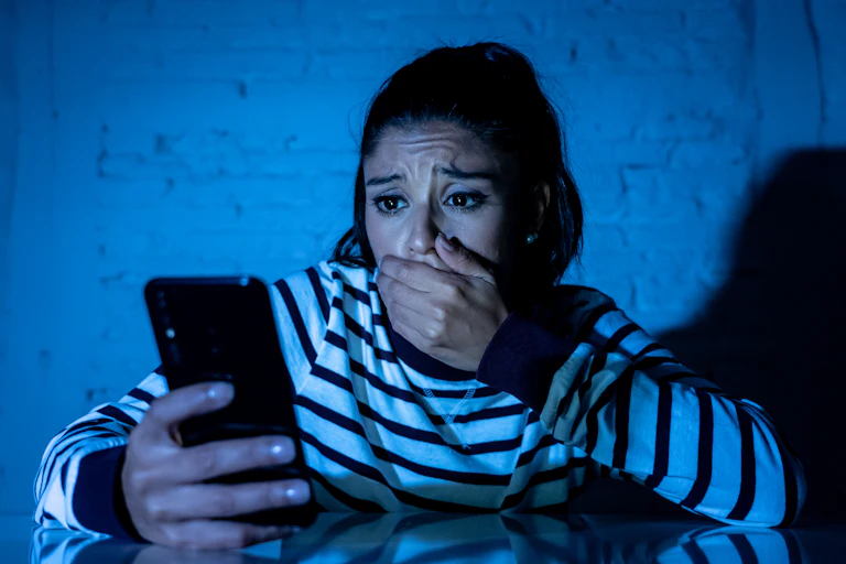 Horrified young woman puts hand over her mouth as she receives a troubling phone message
