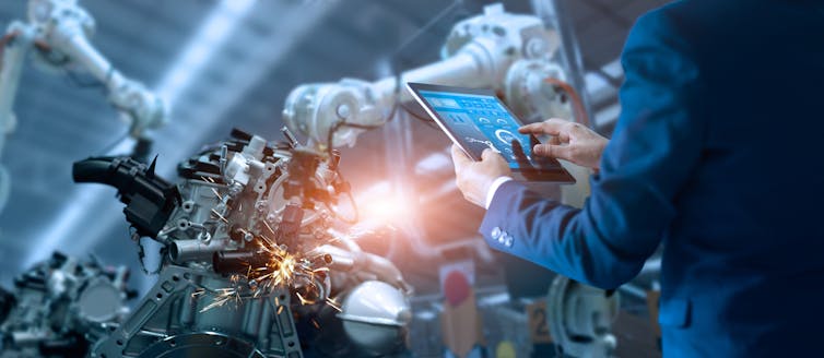 Human with tablet oversees automated machines working in a factory