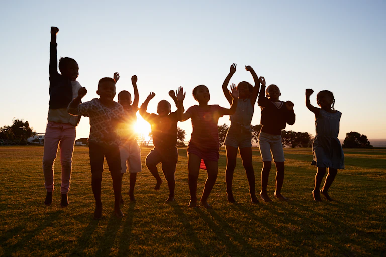 Silhouetted school kids jumping outdoors at sunset.