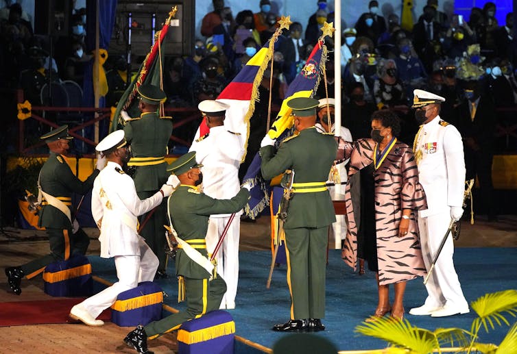 Barbadian president, Sandra Mason, surrounded by military officers in dress uniforms as they raise the flag of Barbados.