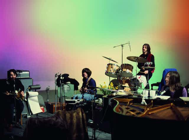 The Beatles peform on a multicolour background. 