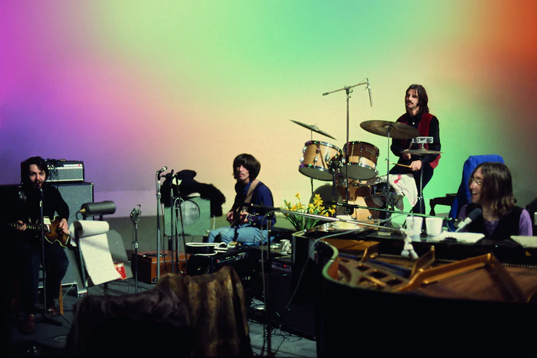 The Beatles peform on a multicolour background.