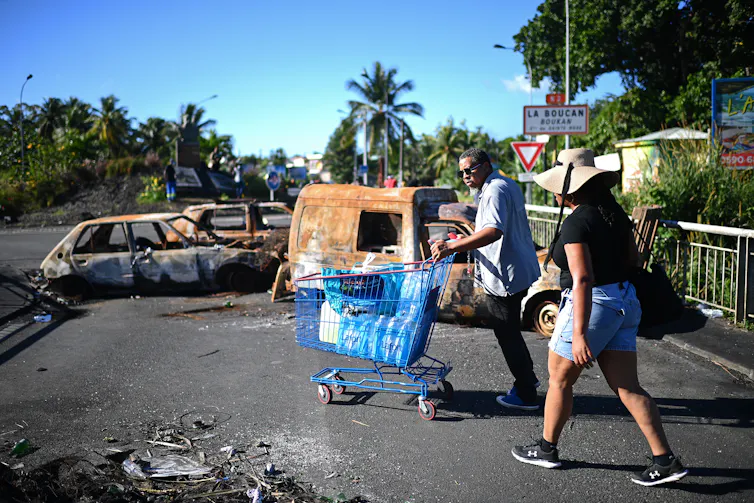 Un homme pousse un chariot à travers un barrage routier fait de véhicules brûlés et de débris, la Guadeloupe, le 29 novembre 2021