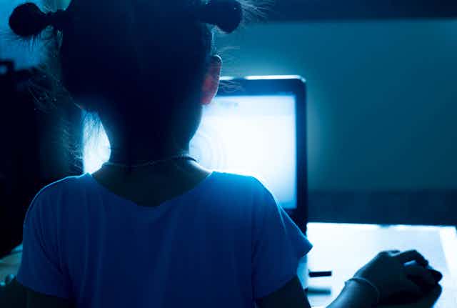 Une petite fille regarde un écran bleu, de nuit.