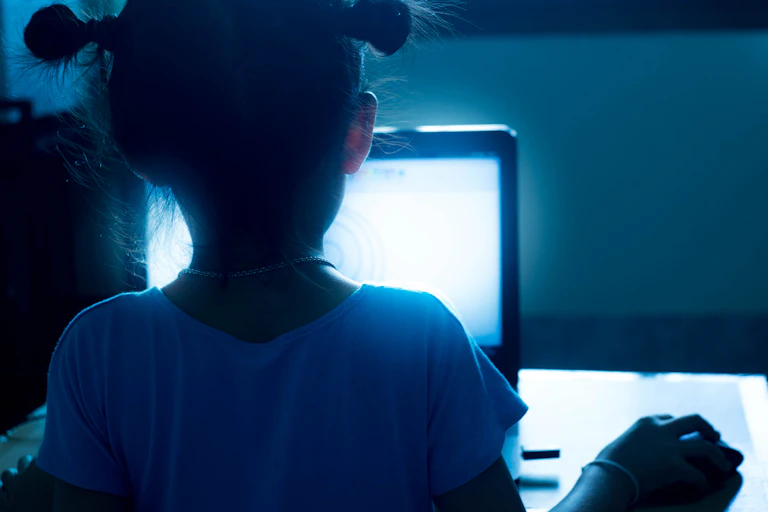 Une petite fille regarde un écran bleu, de nuit.