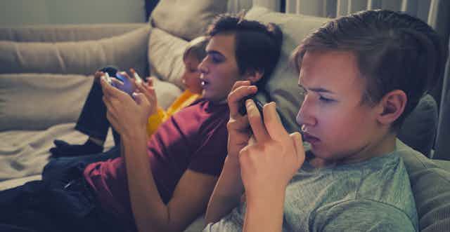 Three brothers of different pre-teen to teen ages are on the couch with devices.