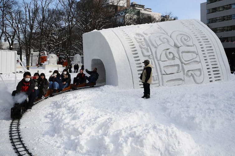 People riding small train through snow tunnel.
