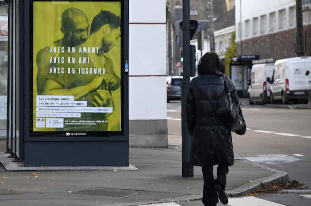 Scène de rue avec en fond une affiche de campagne de prévention du VIH