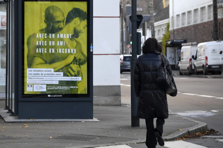 Scène de rue avec en fond une affiche de campagne de prévention du VIH