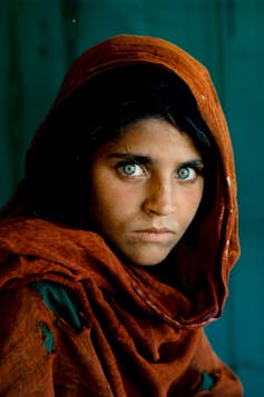 A girl with piercing green eyes wearing a head scarf stares at the camera.