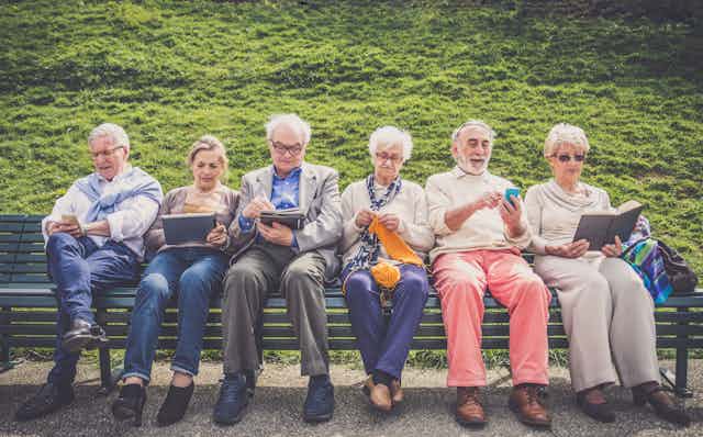 Group of seniors on a bench reading and knitting.