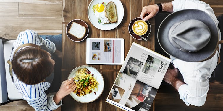 Overheat shot of couple eating breakfast or brunch at a cafe, while reading