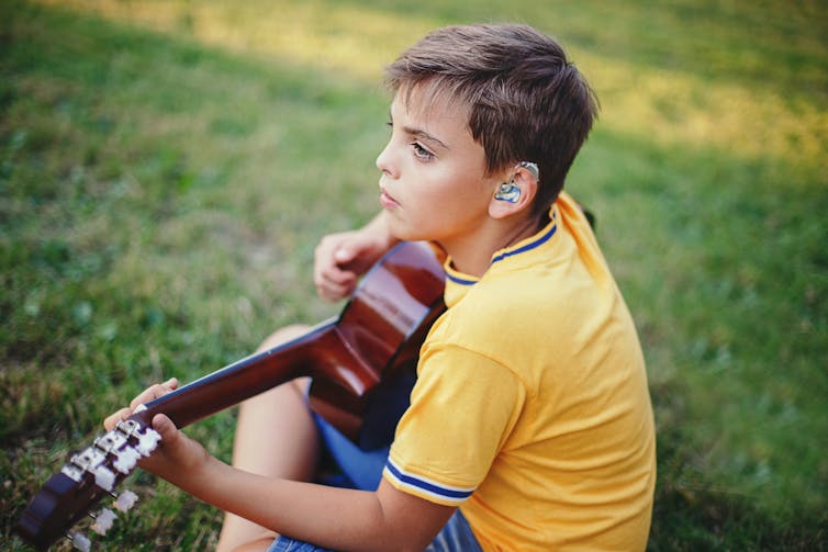 A boy with a blue hearing aid plays guitar