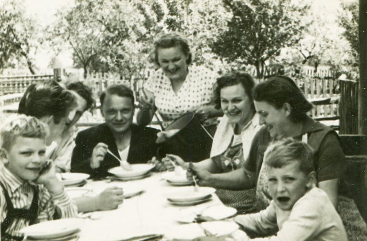 A black and white vintage photo of a large family eating dinner outdoors.