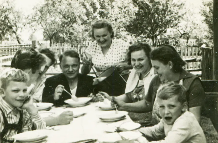 A black and white vintage photo of a large family eating dinner outdoors.