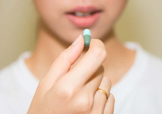 Young woman holding capsule in hand about to swallow