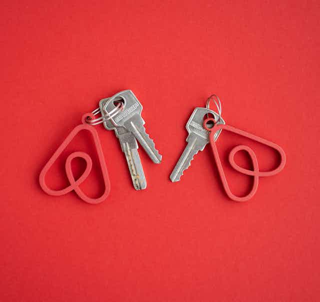Two sets of keys with keychains in the shape of the Airbnb logo against a red background