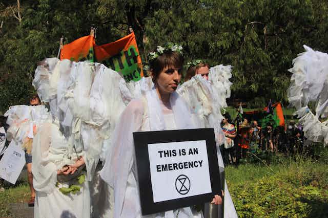 A person holds a sign reading 'This is an emergency'