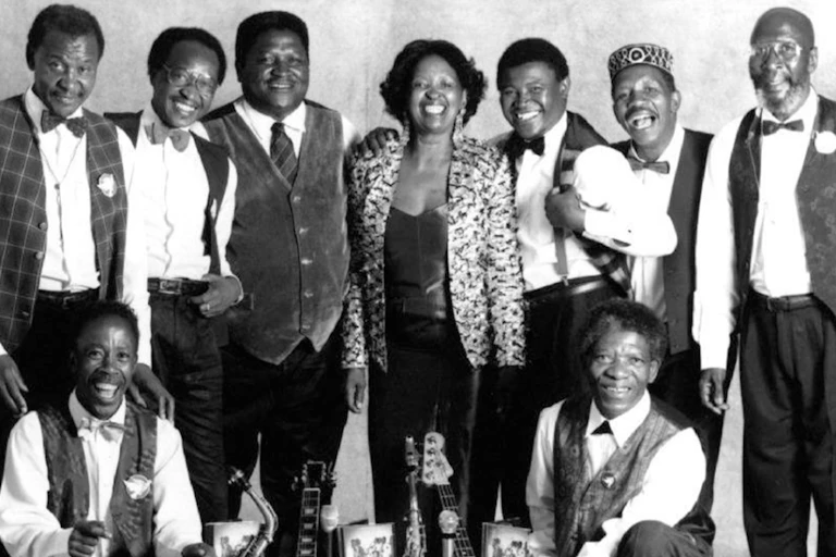 A woman smiles, surrounded by male musicians.