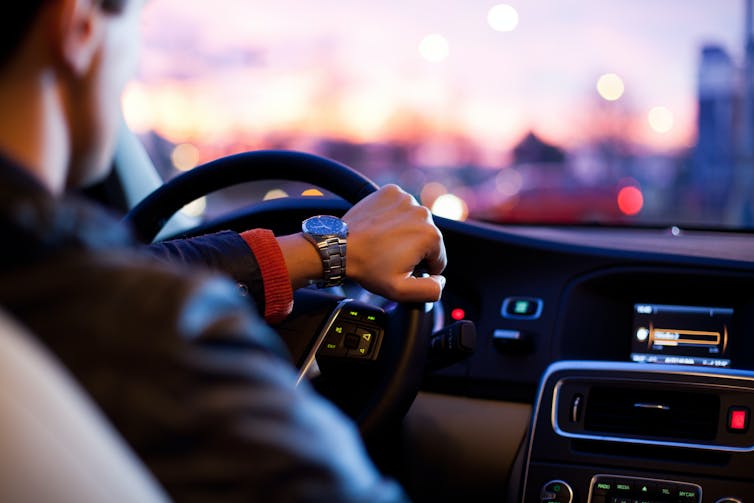 Driver in black leather jacket and with big silver watch at wheel of car